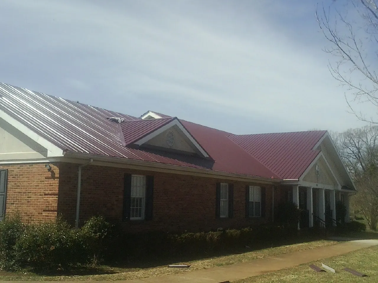 Red metal roof with gabled entries on a long brick building, from a Hail Damage Roof Repair job in Rush