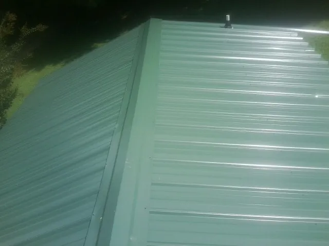 New green metal panels meeting at the ridge of a roof — Flat Roof Repair work by our crew in Rush