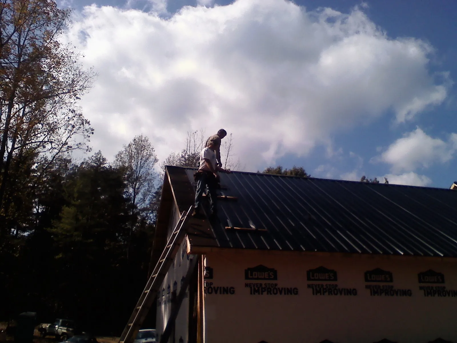Roofer fastening dark metal panels high against a cloudy sky, from a Roof Inspection job in Rush